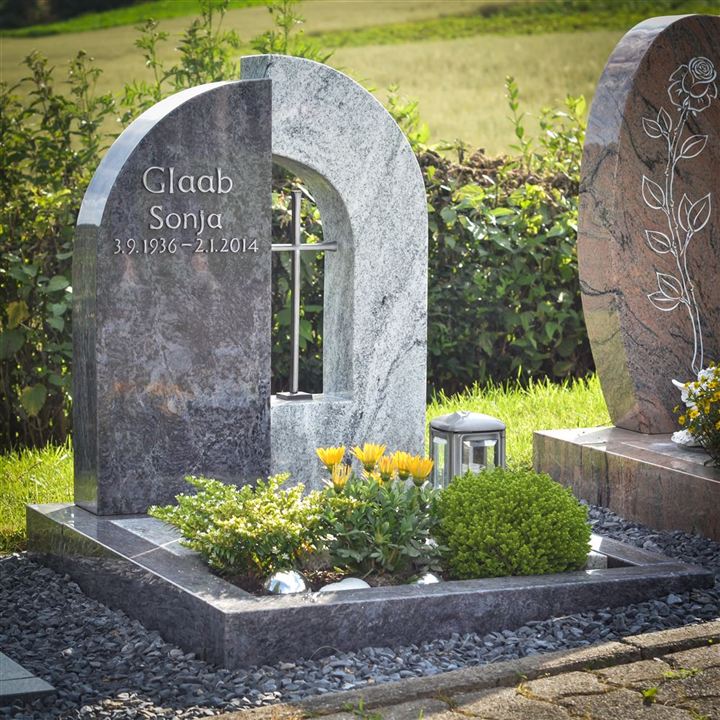 Ein Grabmal aus grauem und weißem Stein mit einem silbernen Kreuz.