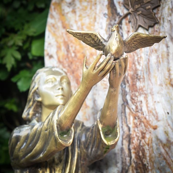 Eine Skulptur einer Frau die eine Taube fliegen lässt. Die Skulptur ist aus Metall