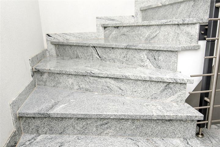 Eine moderne Natursteintreppe aus hellgrauem Naturstein mit Metallgeländer.